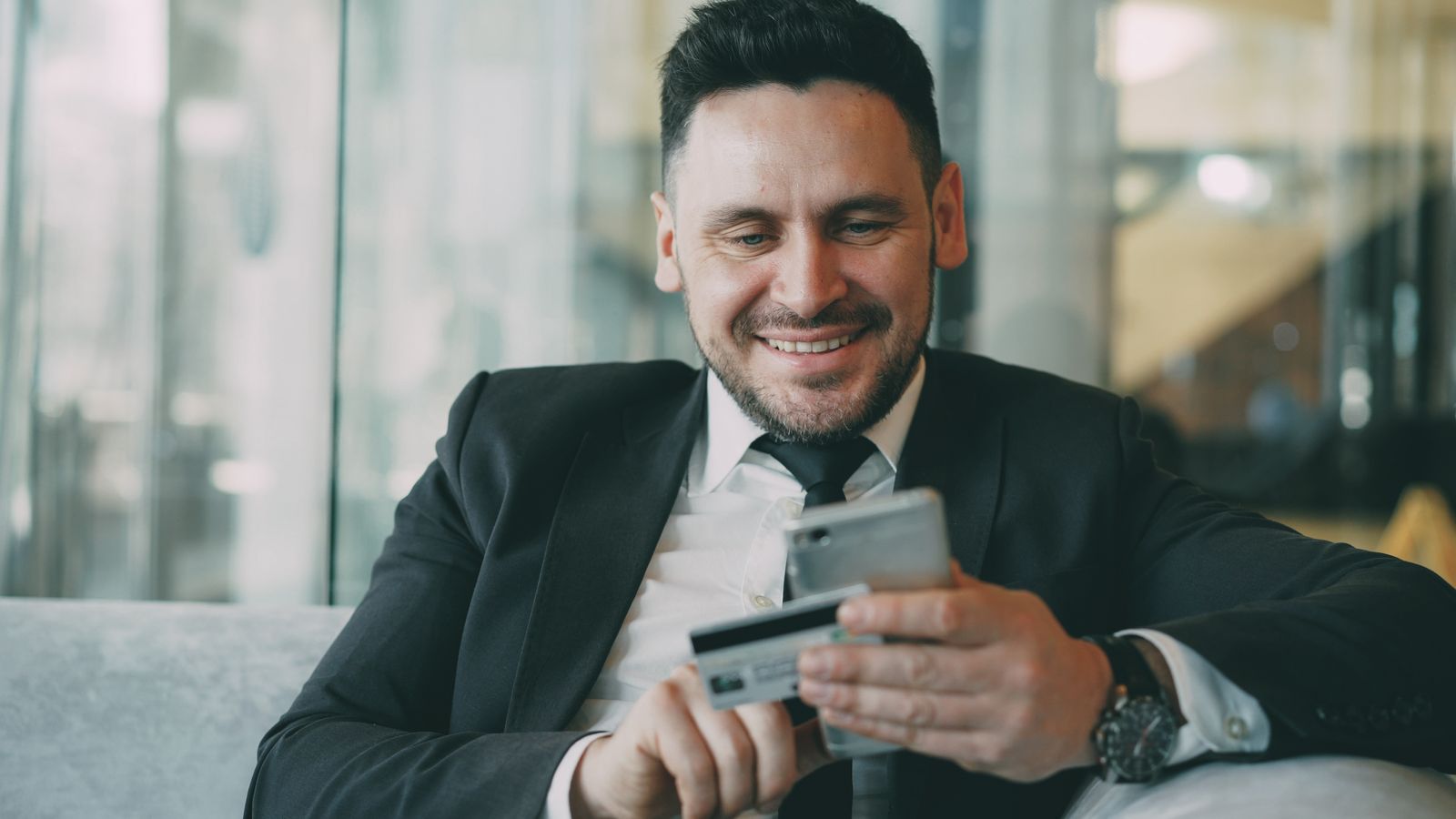 Hombre revisando un pago en su teléfono con la tarjeta en la mano