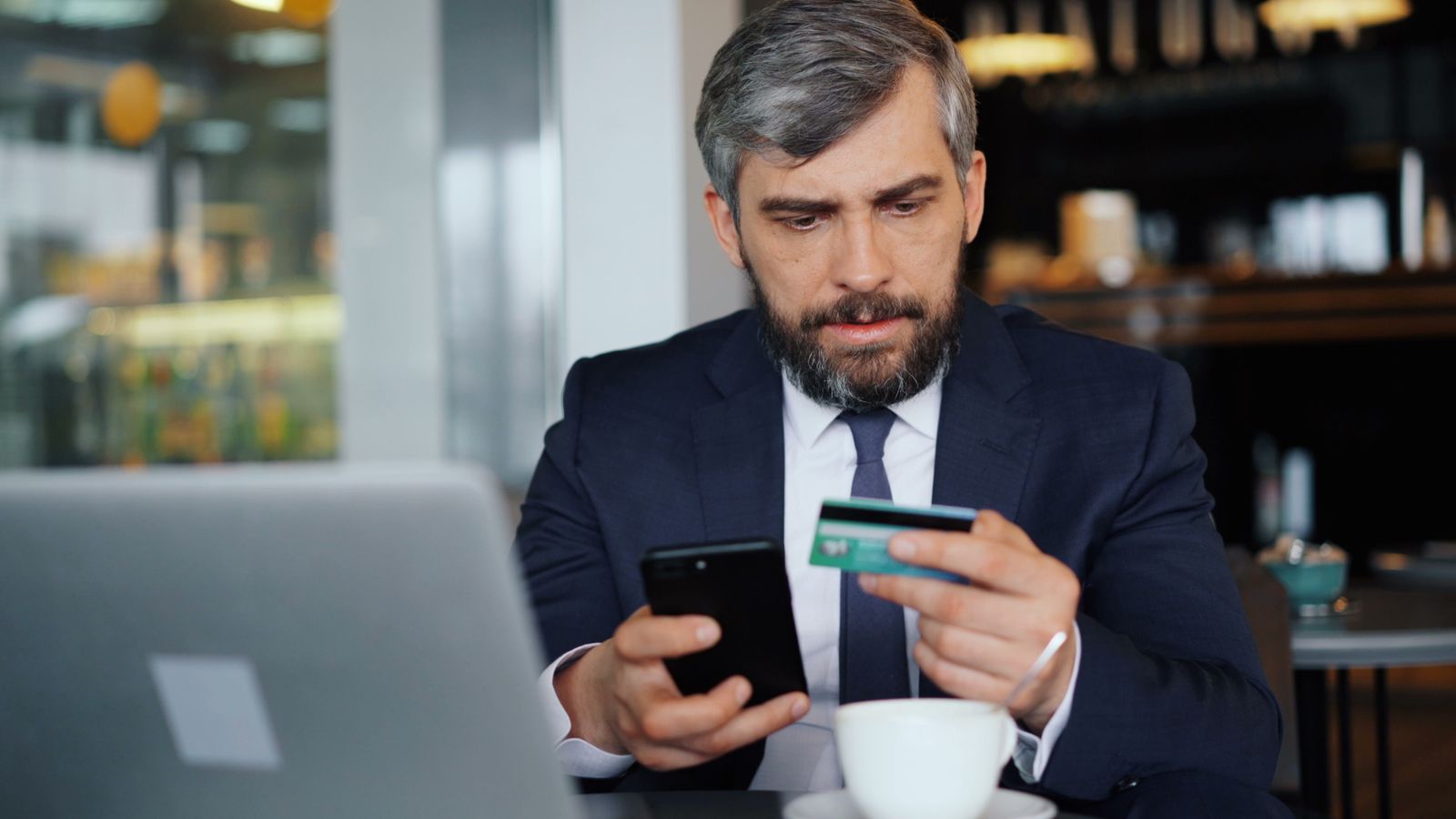 Hombre revisando su cuenta en el teléfono con una tarjeta en la mano
